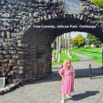 Tessa, mic in hand, stands in front of the memorial arch at Jellicoe Park, Onehunga